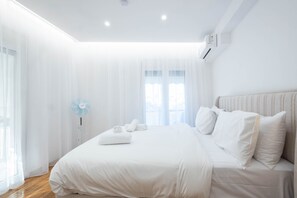 Ein modernes Hotelzimmer mit einem großen Bett, einem Nachttisch und einem Fenster mit leichtem Vorhang.