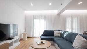 Una sala moderna con un televisor de pantalla plana, un sofá, una mesa de centro y una mesita auxiliar.