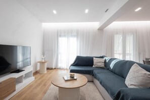 Ein modernes Wohnzimmer mit Flachbildfernseher, Sofa, Couchtisch und einem kleinen Beistelltisch.