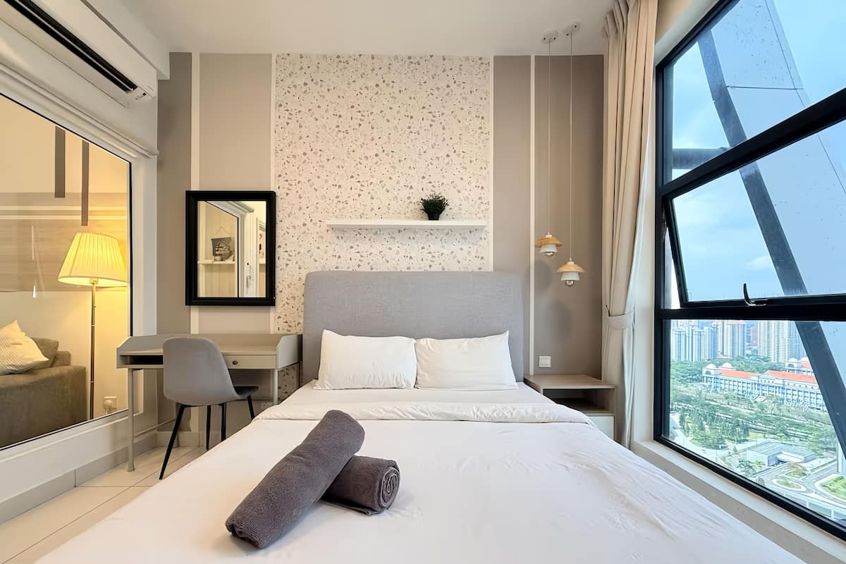 A hotel room with a bed, a desk, a chair, a large window with a city view, and a wall with a speckled pattern.