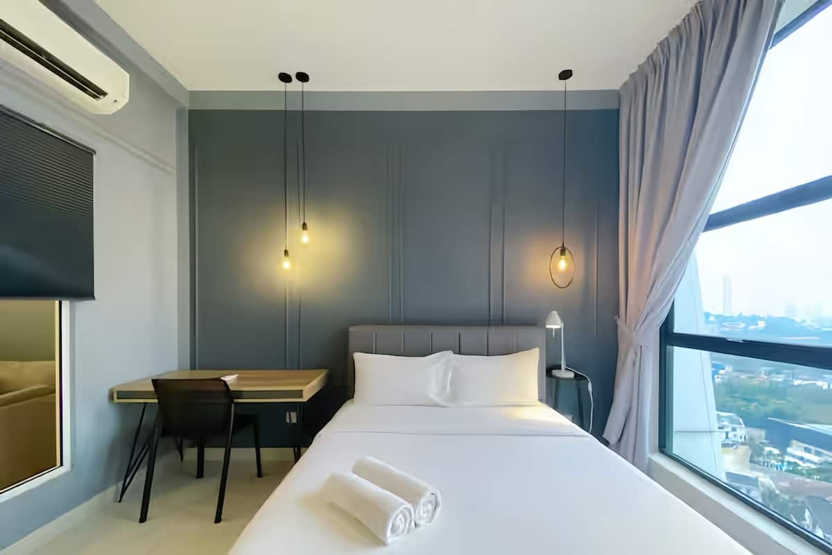 A hotel room with a bed, a desk, a chair, a lamp, and a large window.