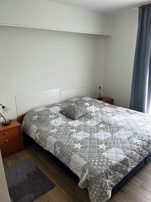 A neatly made bed with a star-patterned quilt, a bedside lamp, and a small rug on a wooden floor. - First floor apartment 3 bedrooms rural location (Malente)
