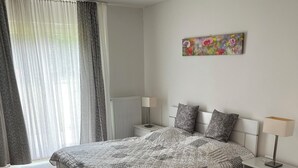 Une chambre à coucher avec un grand lit, des tables de chevet, un radiateur, une fenêtre avec des rideaux et un tableau au mur.