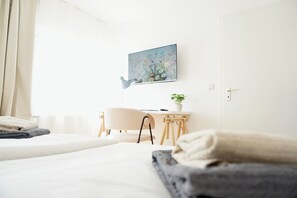 Habitación de hotel con cama, escritorio, silla, un cuadro en la pared y una planta en maceta.