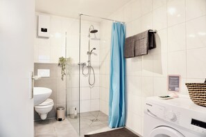 Een moderne badkamer met een douchecabine van glas, een wit toilet, een wasmachine en een handdoekrek.