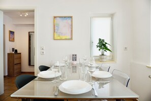 Een eetgedeelte met een glazen tafel voor vier personen, stoelen, een kamerplant en een schilderij aan de muur.