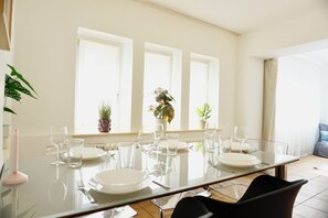 Comedor con mesa de vidrio, sillas y plantas en macetas.
