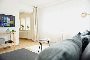 Un dormitorio moderno con una cama, un escritorio con ordenador, un radiador y una ventana con cortinas.