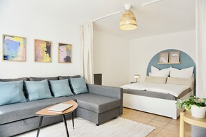 Een moderne slaapkamer met een grijze bank, een nachtkastje, een bed met een blauwe hoofdbord en drie abstracte schilderijen aan de muur.