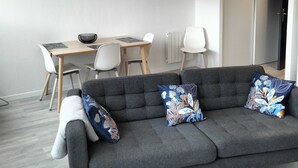 A modern living room with a grey sofa, two patterned cushions, a dining table with chairs, a hanging light fixture, and a painting on the wall. - Apparently T2 45 m2, Vallières district  (Clermont-Ferrand)