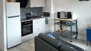 A modern kitchen with white cabinets, a black oven, and a microwave on a wooden shelf. - Apparently T2 45 m2, Vallières district  (Clermont-Ferrand)