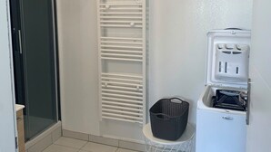 A small, clean room with a white radiator, a washing machine, and a basket on the floor. - Apparently T2 45 m2, Vallières district  (Clermont-Ferrand)