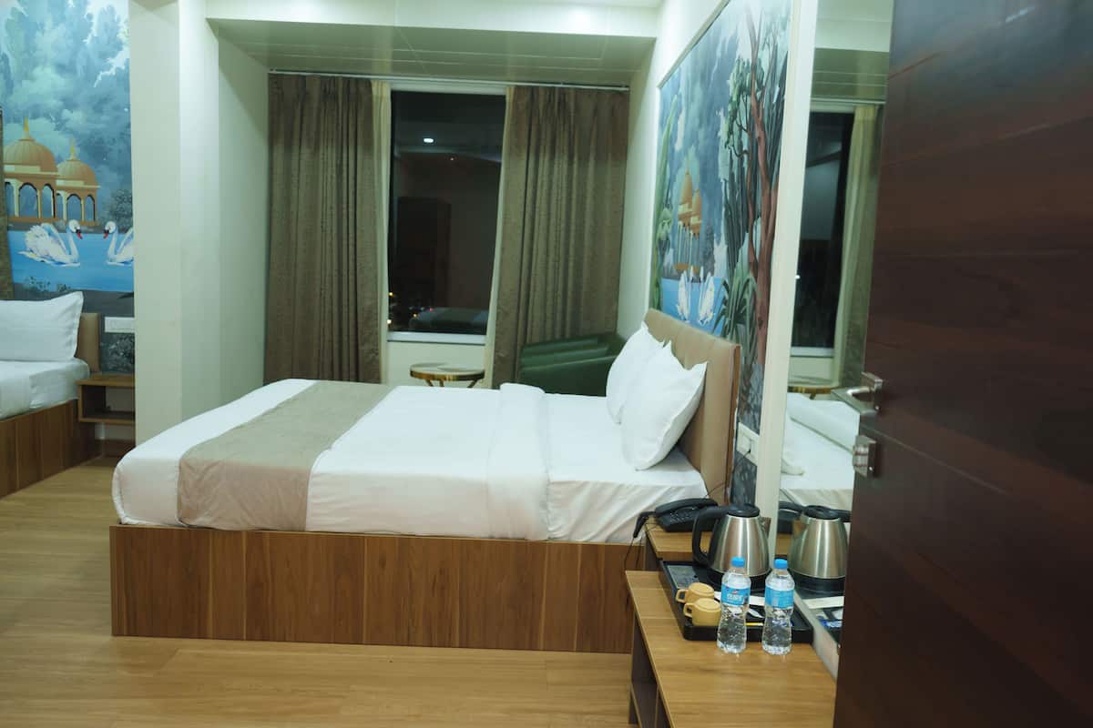 A hotel room with a large bed, a desk with a telephone and coffee maker, a window with curtains, and a painting on the wall.