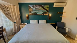 Ein Hotelzimmer mit Bett, Schreibtisch, Stuhl, einem Bild an der Wand und einer Klimaanlage.