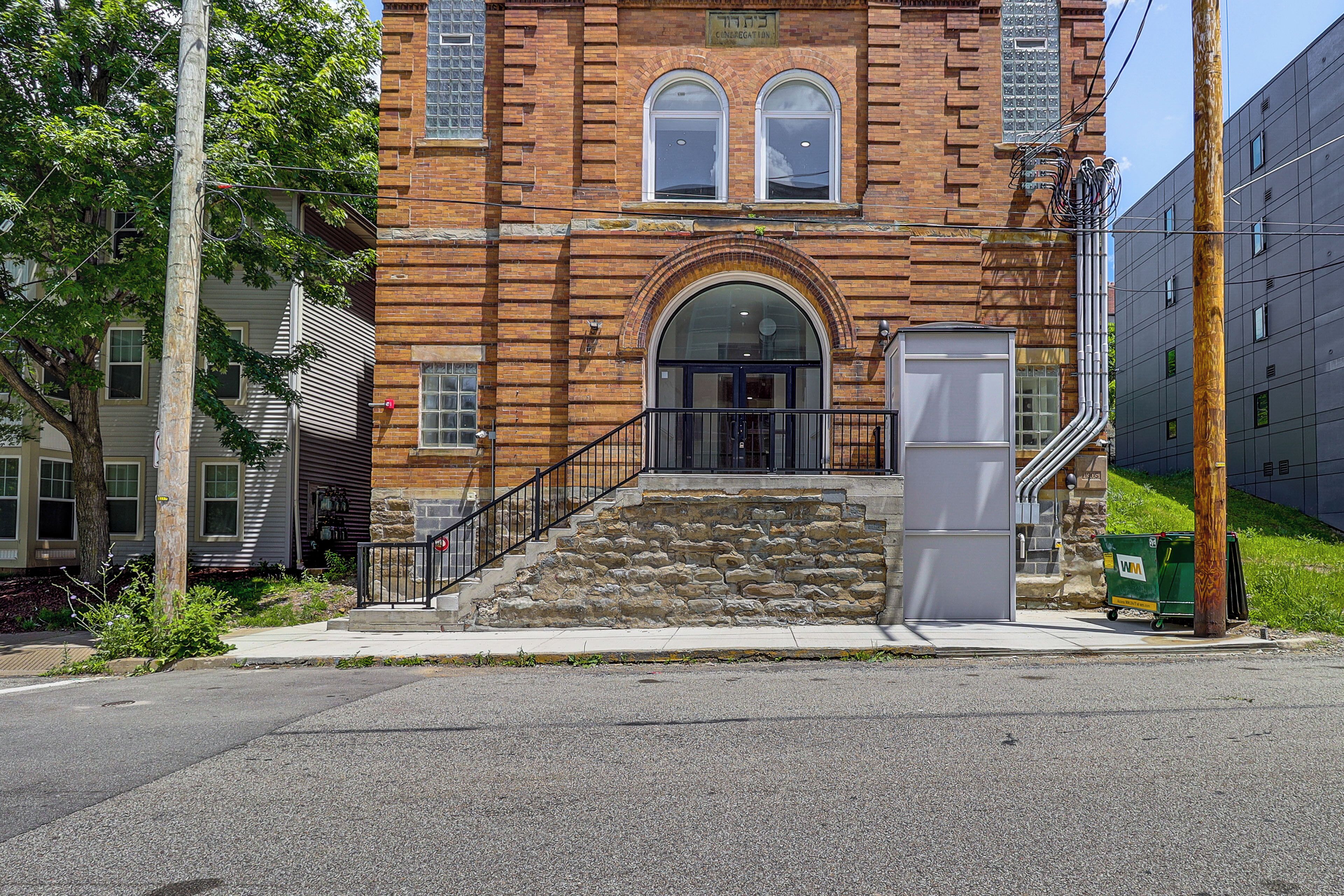 A brick building with a central arched entrance, a stone staircase, and a sidewalk leading to the entrance.