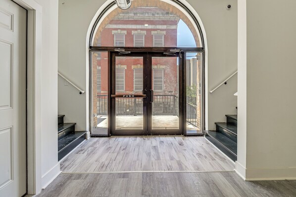 A hallway with a double door leading to an outdoor area, a staircase, and a view of a brick building.