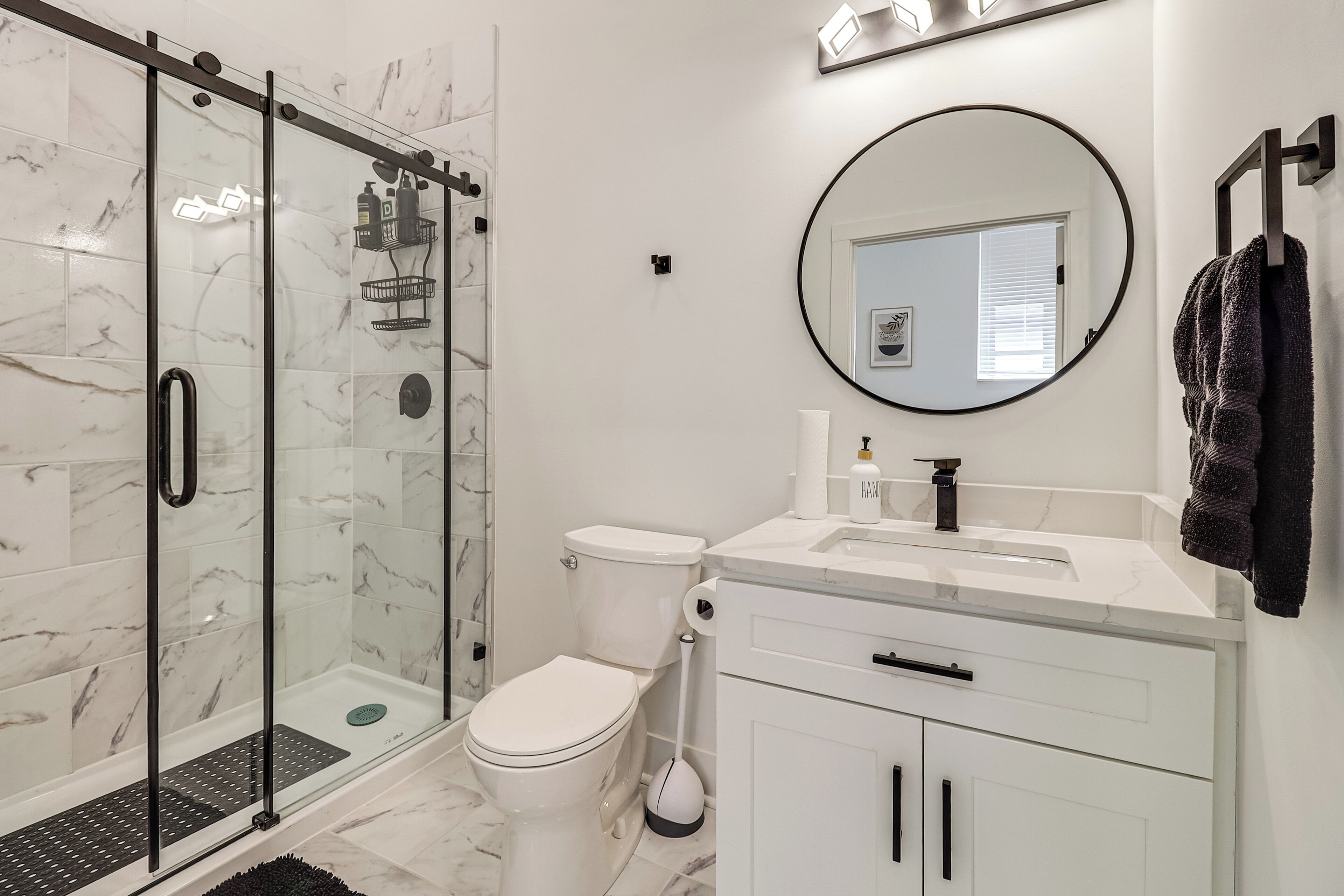 A modern bathroom with a glass shower enclosure, a toilet, a sink with a mirror, and a towel rack.