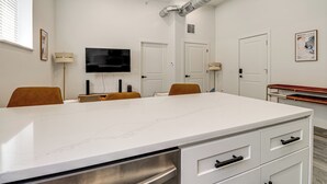 Una cocina moderna con una isla grande, muebles blancos y un televisor de pantalla plana montado en la pared.
