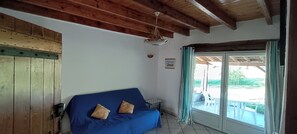 A room with a wooden ceiling, a blue sofa with cushions, a small table, and a view through a glass door to an outdoor area. - Countryside cottage, private terrace & garden overlooking walnut & plum orchards (Penne-d'Agenais)