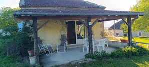 A covered outdoor seating area with a table and chairs, a potted plant, and a building with a tiled roof. - Countryside cottage, private terrace & garden overlooking walnut & plum orchards (Penne-d'Agenais)