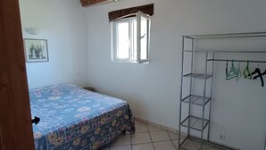 A bedroom with a bed, a wardrobe, a window, and a wall-mounted shelf.