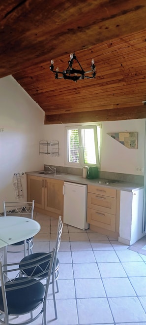 Une cuisine avec des meubles en bois, un réfrigérateur blanc, un évier et un coin repas avec des chaises et une table en métal.