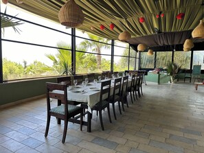 A restaurant with a long table set for dining, large windows, and hanging light fixtures. - Grotte de Sel Private pool (Ghar al Milh)