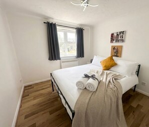 A bedroom with a bed, a window with curtains, a wall with a poster, and a wooden floor. - Keepers Court Luxury Stay (South Croydon)