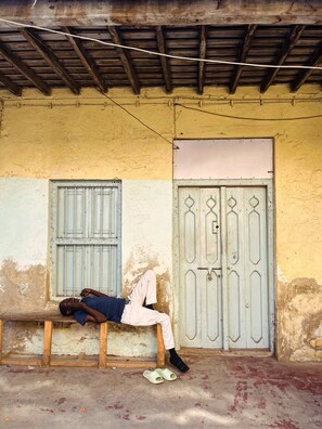 A person resting on a bench outside a building with a wooden ceiling and a door with decorative metalwork. - Azure Chameleon House (Zanzibar)