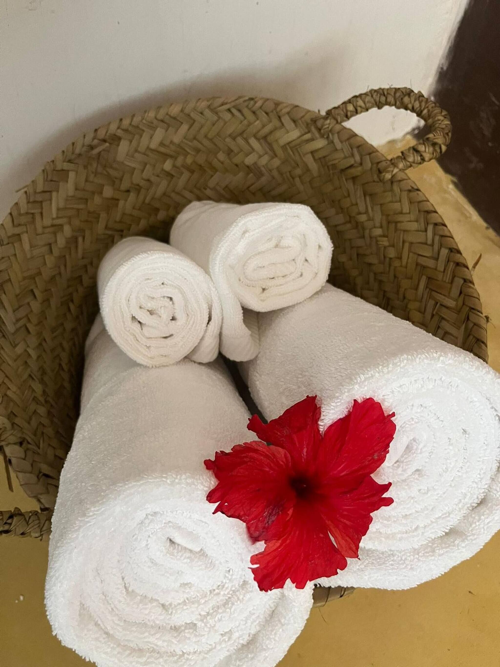 A woven basket containing rolled white towels and a red hibiscus flower.