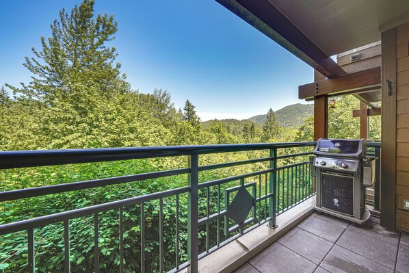 Un balcon avec un barbecue, une vue sur une forêt et une montagne à l’horizon.