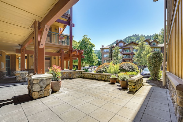 A hotel courtyard with stone planters, a wooden pergola, and a view of other buildings and trees.