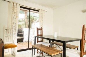 Une pièce comprenant une table à manger, des chaises, un banc et une porte-fenêtre coulissante donnant sur un espace extérieur.