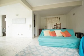 Una stanza con un letto ricoperto da una coperta color petrolio, una parete bianca con un quadro incorniciato e un tappeto decorato.