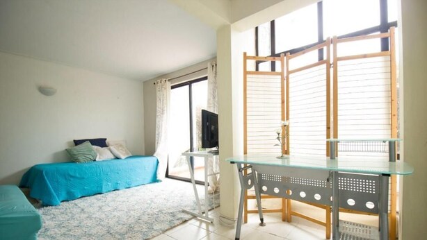 A bedroom with a bed, a desk, and a window with blinds.