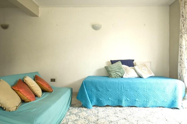 Une chambre avec deux lits, chacun recouvert d’une couvre-lit de couleur différente, et un tapis de couleur claire.