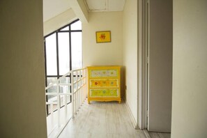 Un couloir avec une commode jaune, une rambarde blanche et une fenêtre.
