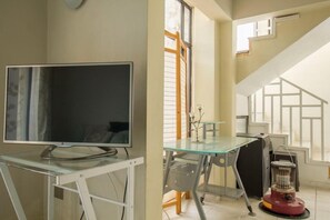 Quarto com televisão sobre uma mesa de vidro, janela com persianas e escada com design geométrico.