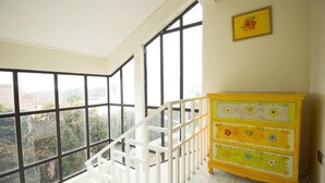 A room with a white staircase, large windows, and a yellow dresser.