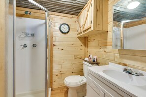 Un baño de cabaña de madera con ducha, inodoro, lavamanos y un reloj en la pared.