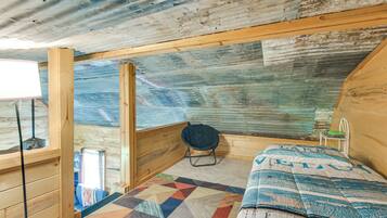 Una cabaña con interior de madera, una cama acolchada, una silla y un ventanal.