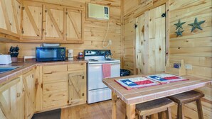 Cocina de cabaña de madera con microondas, estufa, refrigerador y una mesa con colcha.