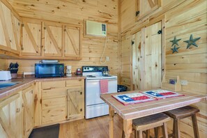 A wooden cabin kitchen with a microwave, stove, refrigerator, and a table with a quilt.