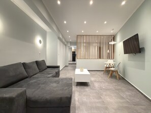 A modern living room with a grey sectional sofa, a white coffee table, and a dining area with a white table and chairs. - SmartLiving Central Apt 11 (Thessaloniki)