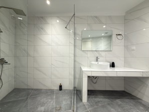 Een moderne badkamer met een douchecabine van glas, een witte wastafel en een wand betegeld met marmer.