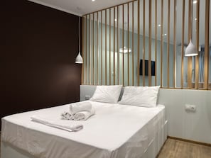 Une chambre d’hôtel moderne avec un lit bien fait, une cloison en bois et un téléviseur fixé au mur.