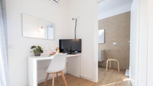 Una camera moderna con una scrivania bianca, una sedia, una televisione, una pianta in vaso e uno sgabello.