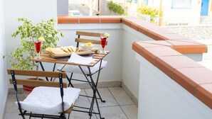 Un balcone con due sedie, un tavolo con cibo e bevande, e una pianta in vaso.