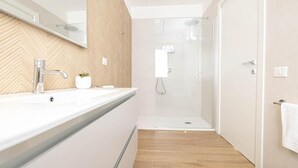 Un bagno moderno con doccia, lavandino con specchio e una pianta in vaso.