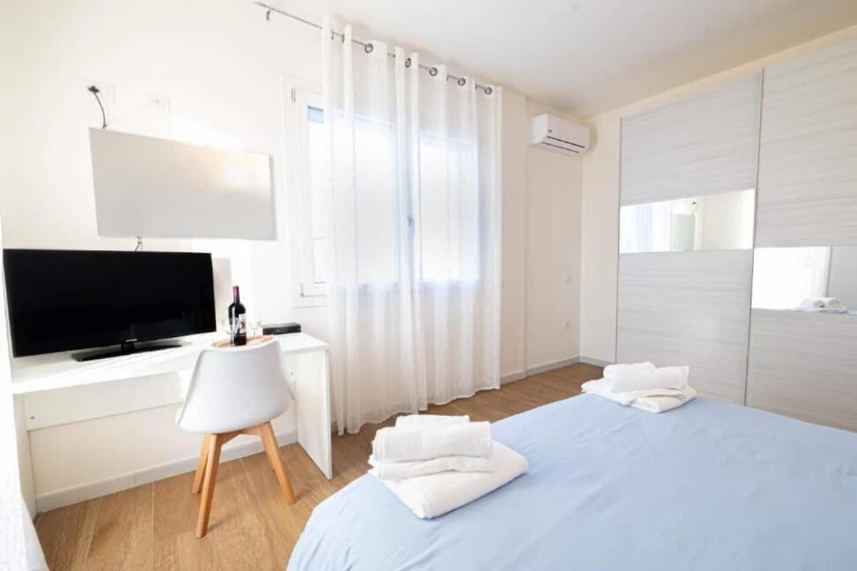 Ein Hotelzimmer mit Bett, Schreibtisch mit Fernseher, Stuhl und einem Fenster mit Vorhängen.